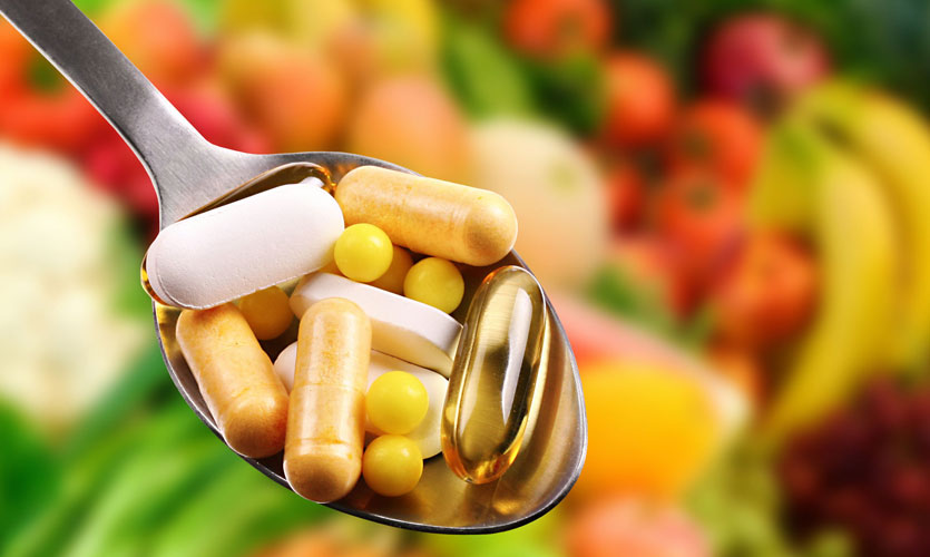 A spoon with various supplements, with fruit in the background